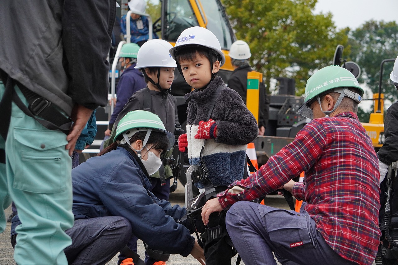 高所作業車の体験に向け、安全帯を装着する児童。社員が一人ひとりに声をかけながら、安全確認を行った